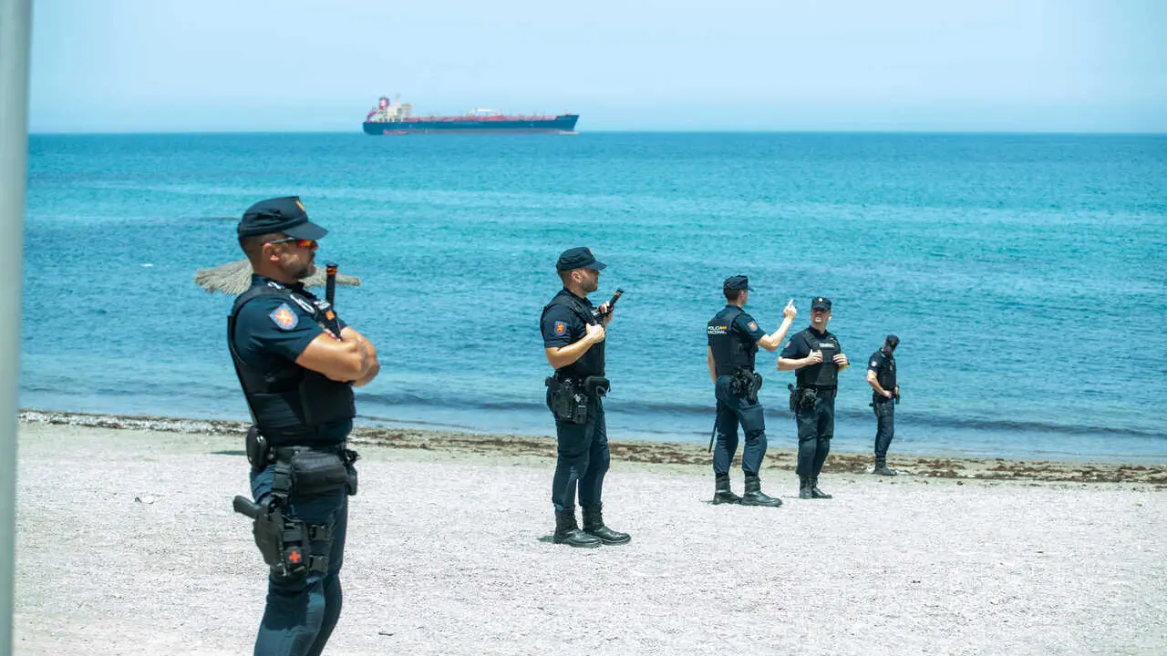 Spanish National Police officers stand around a large group of migrants near the Temporary Stay Centre for Immigrants (CETI).
